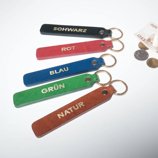 Fünf handgefertigte LoveTag Leder-Schlüsselanhänger in den Farben Schwarz, Natur, Grün, Rot und Blau mit edler Goldprägung in einer Fächer-Anordnung. Authentic Style Photografie mit Blitz
