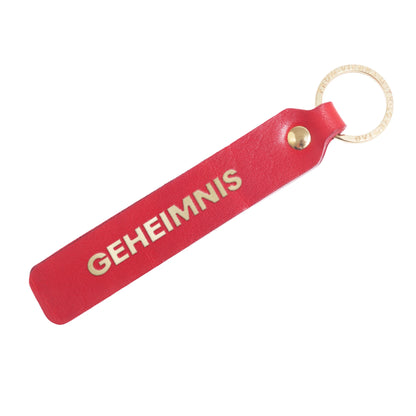 Flatlay, Schlüsselanhänger aus Leder in Rot mit Goldprägung 'Geheimnis' von LoveTag, handgefertigt in Wien