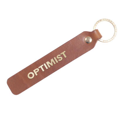Flatlay, Schlüsselanhänger aus Leder in Natur mit Goldprägung 'Optimist' von LoveTag, handgefertigt in Wien