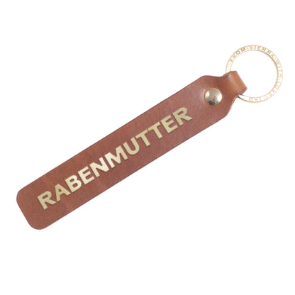 Flatlay von einem Schlüsselanhänger aus Leder in Natur mit Goldprägung 'Rabenmutter' von LoveTag, handgefertigt in Wien