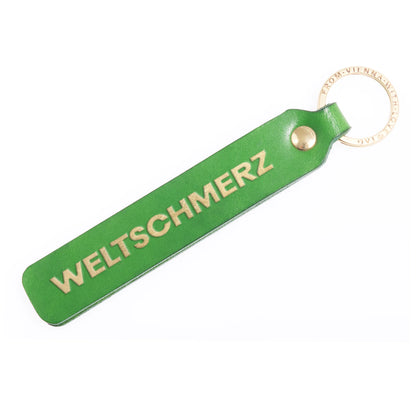 Flatlay, Schlüsselanhänger aus Leder in Grün mit Goldprägung 'Weltschmerz' von LoveTag, handgefertigt in Wien