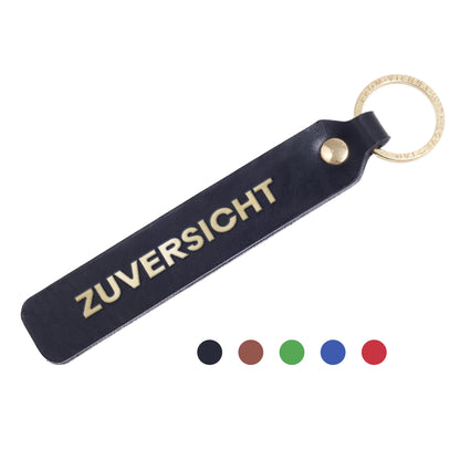 Flatlay, Schlüsselanhänger aus Leder in Schwarz mit Goldprägung 'Zuversicht' von LoveTag, handgefertigt in Wien